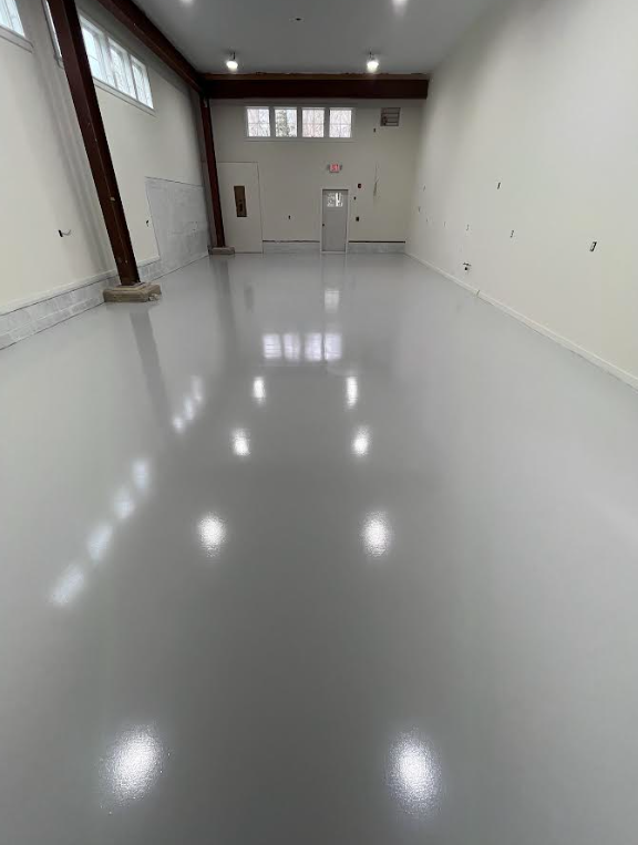 High-gloss solid gray epoxy floor in a bright open commercial room with an exposed beam