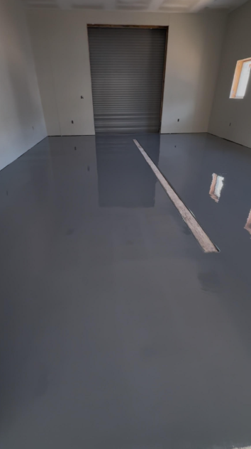Freshly coated solid gray epoxy floor in a commercial unit with a roll-up door
